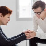 Two individuals in a therapy session at The Guidance House, showing support with clasped hands in a bright, intimate setting.